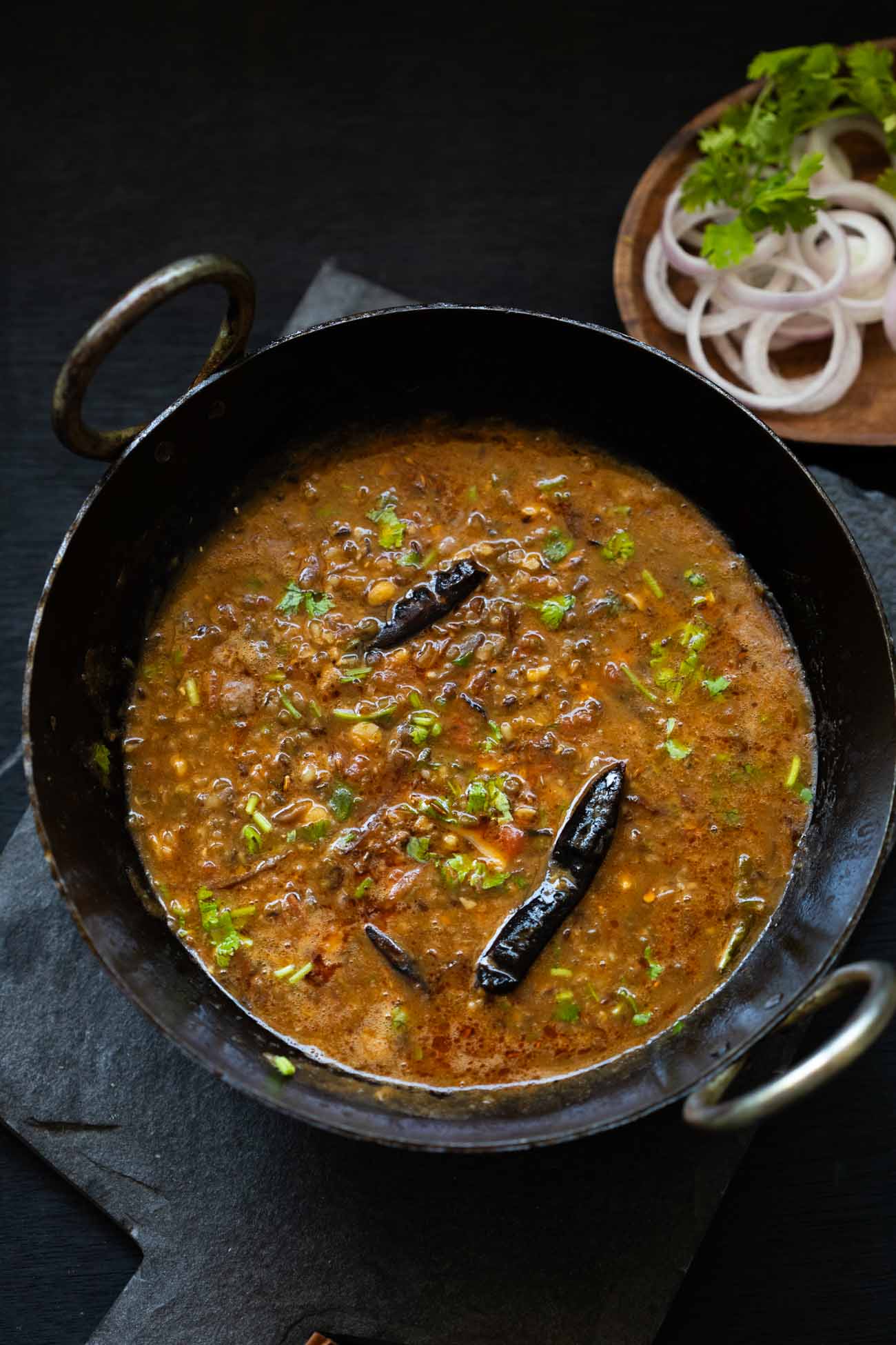 A black kadhai of Dhaba style Mixed Dal with a side of sliced onions in a bowl