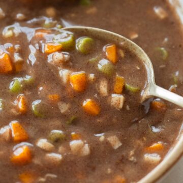a whote bowl with ragi soup with diced carrots and beans with a spoon