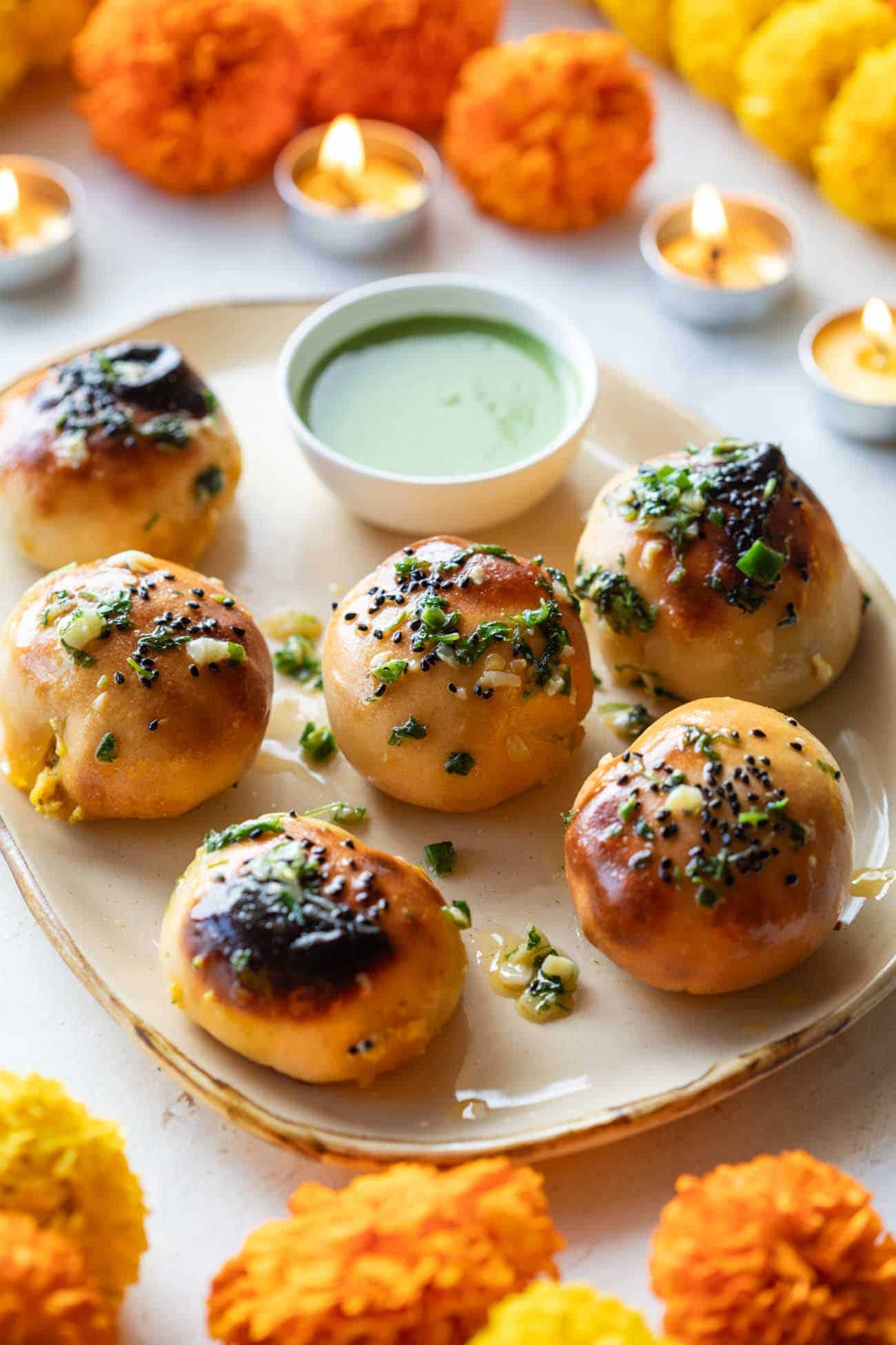 Naan bombs served on a platter with mint chutney and marigold flowers strewn about