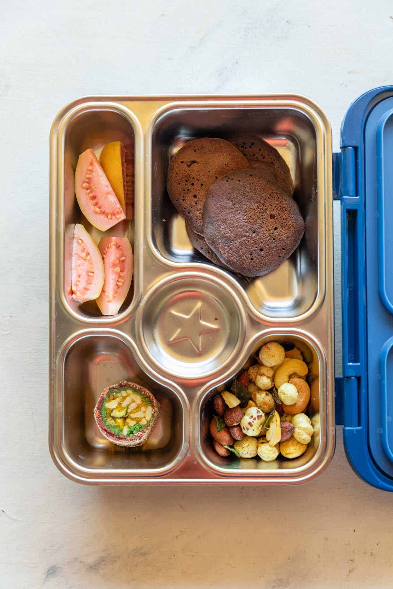 Picture of lunch box with ragi pancakes, guava, roasted makhanas and mithai