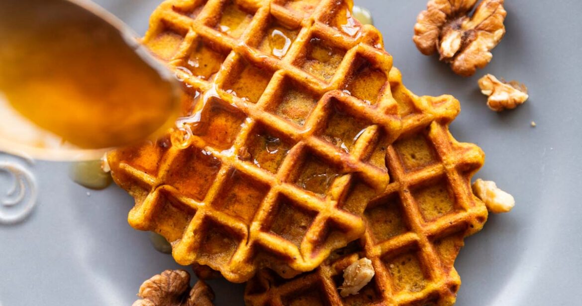 Spoon drizzling honey over two pumpkin waffles served on a plate