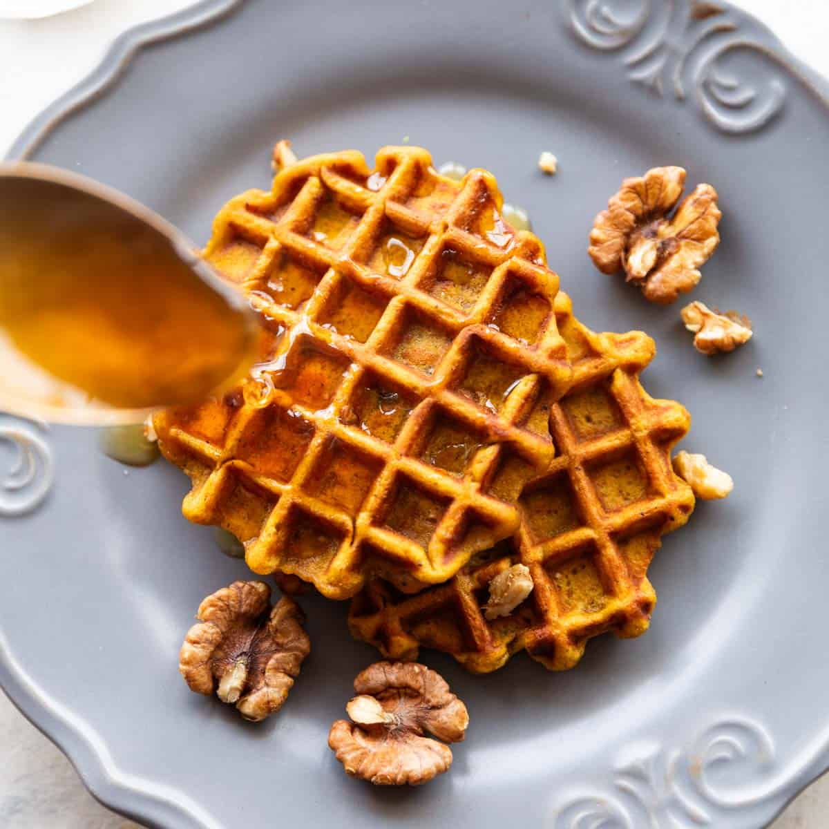 Spoon drizzling honey over two pumpkin waffles served on a plate