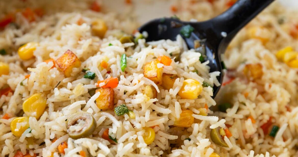 colourful rainbow rice in a white pan with a black rubber spatula
