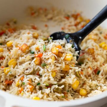 colourful rainbow rice in a white pan with a black rubber spatula