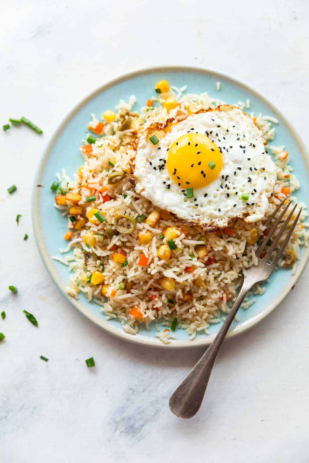 colourful rainbow rice on a blue plate with a sunny side up egg on top