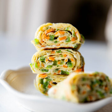 a close up shot of korean omelette roll stacked one on top of the other in a white bowl