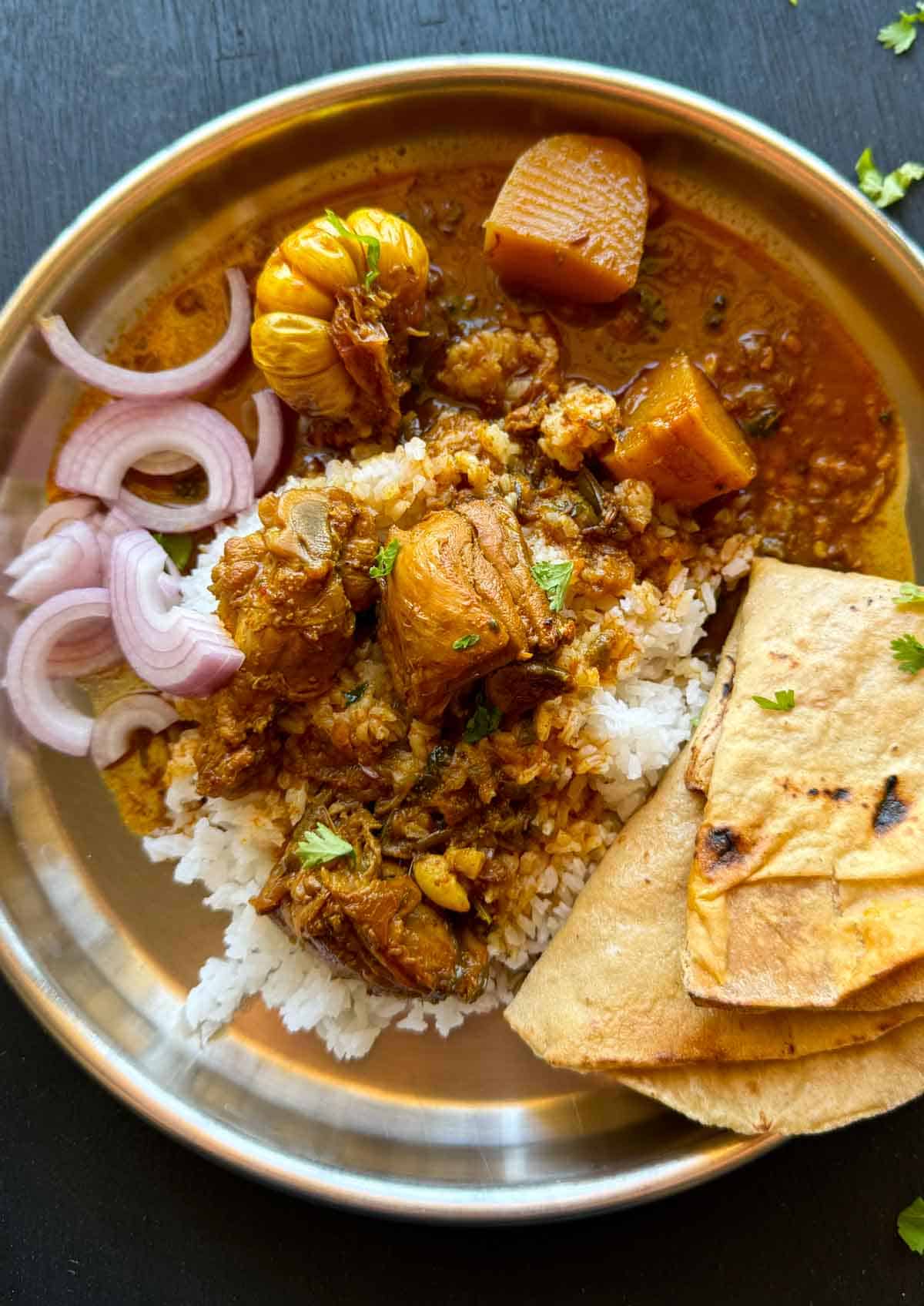 Bihari Chicken curry served on a plate with rice, roti and onions