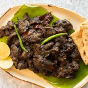 Black sesame chicken served on a platter with rotis and lime