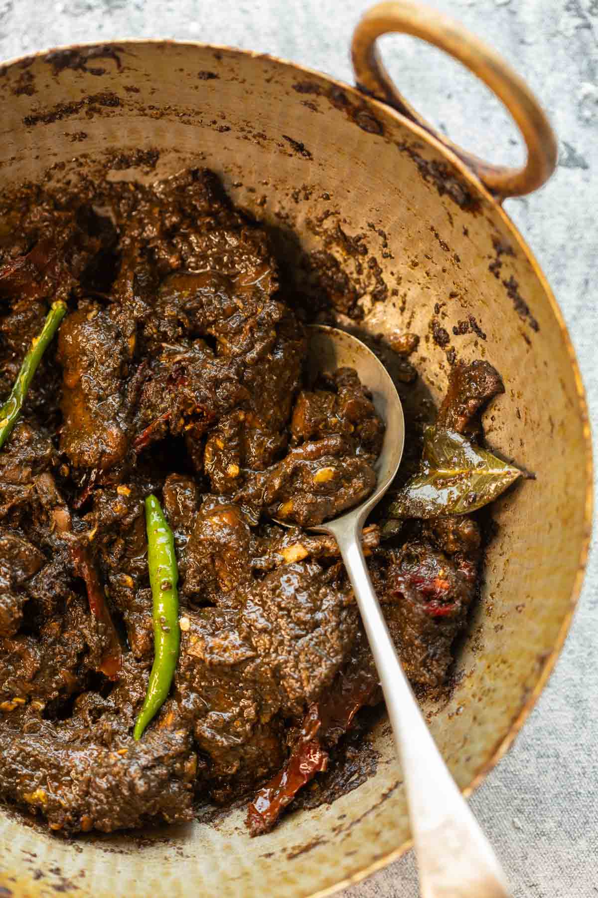 Black sesame chicken curry served in a brass kadhai with spoon