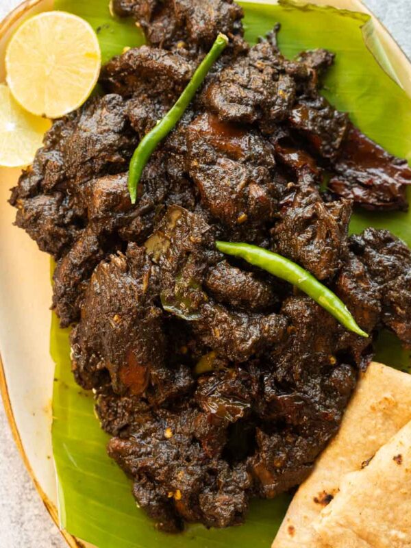 Black sesame chicken served on a platter with rotis and lime