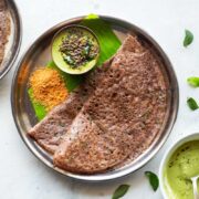 Ragi dosa served in a steel plate on a banana leaf with coconut chutney and podi
