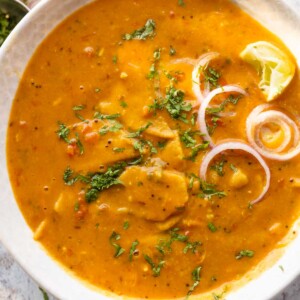 dal dhokli served in a bowl with onion rings and lemon wedges