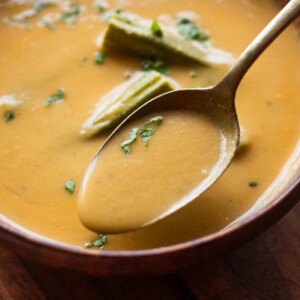 a close up image of drumstick soup garnished with boiled drumsticks and coriander leaves