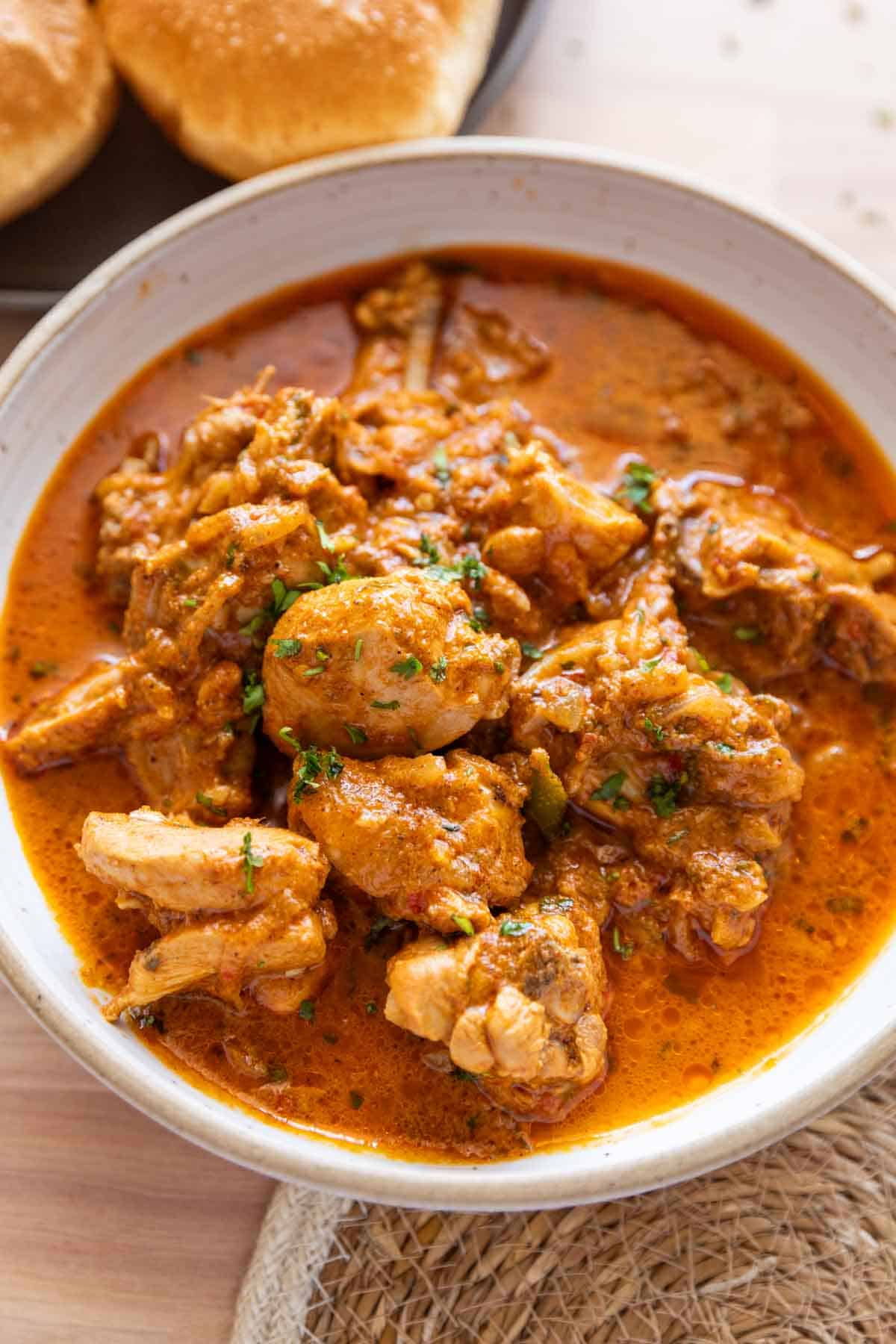 Chatpata dahi chicken in a white bowl with pooris on the side