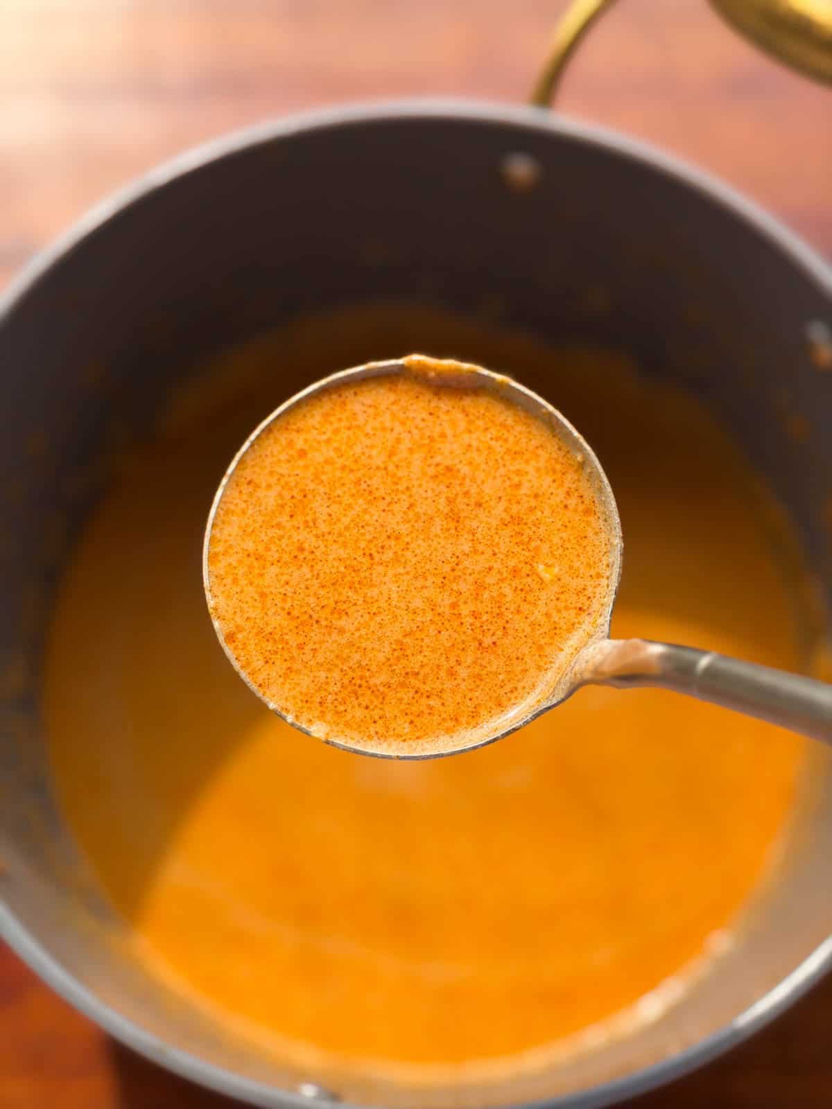 the peanut butter ramen noodle broth scooped up in a ladle to showcase it's smooth texture