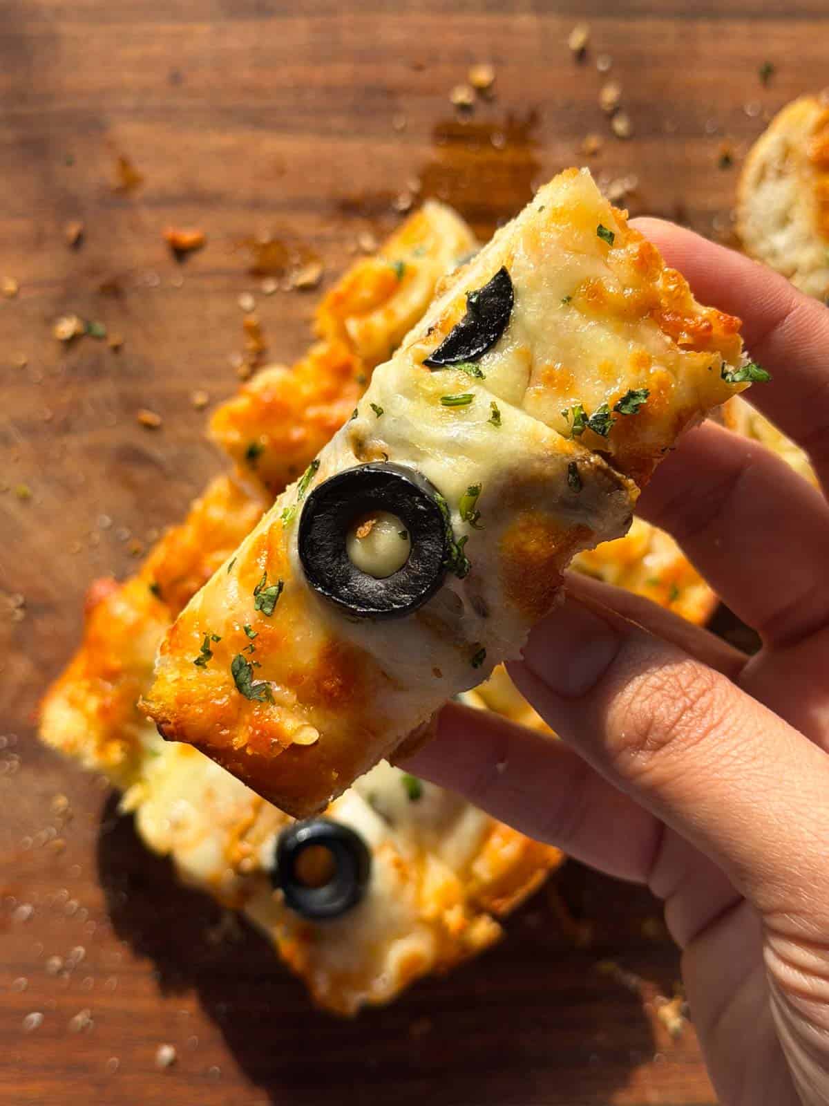 a person holding up a slice of the air fryer pizza garlic bread to showcase it's creamy and crispy texture