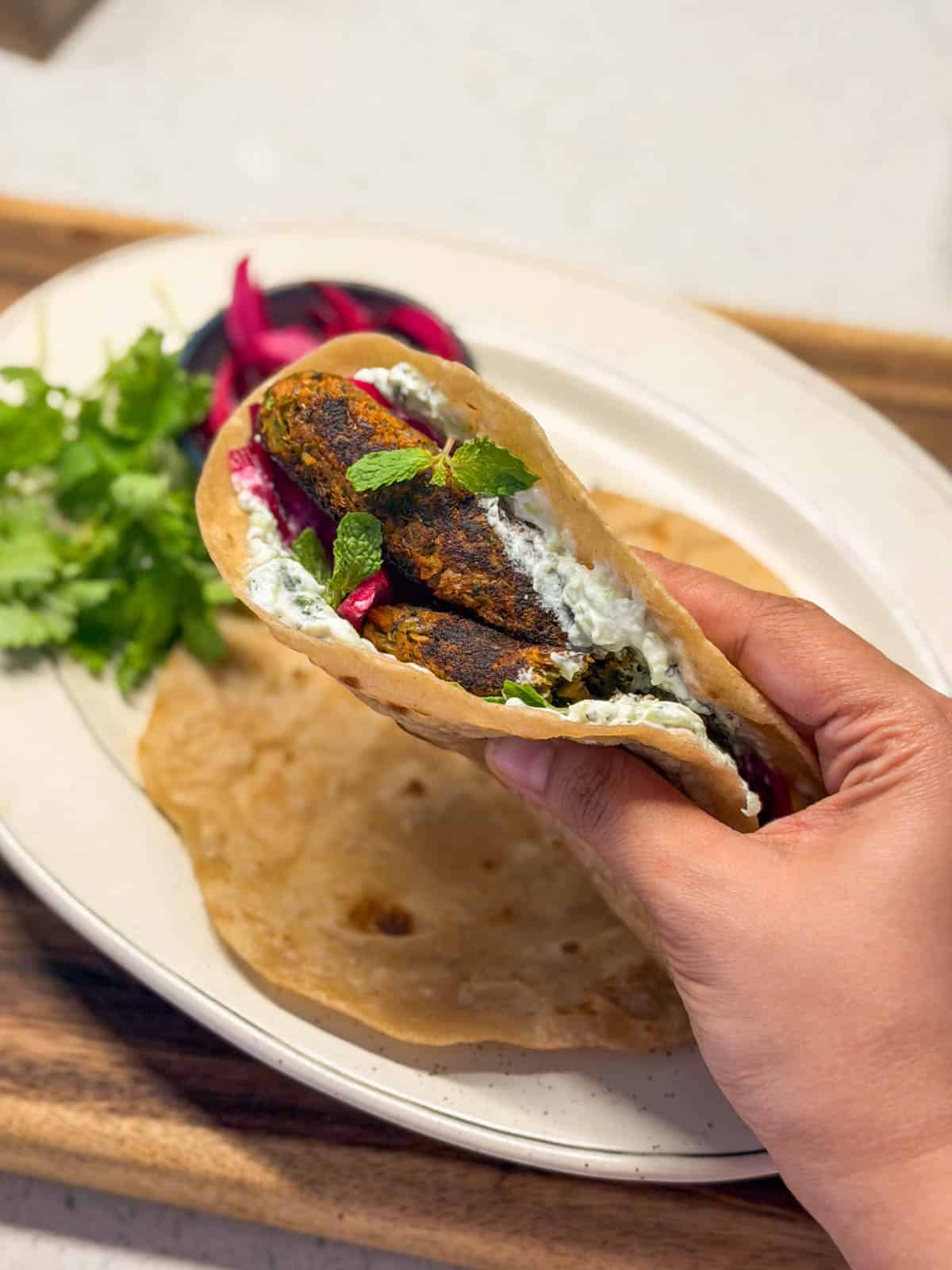 an image of a person holding veg a veg seekh kebab assembled in a roti