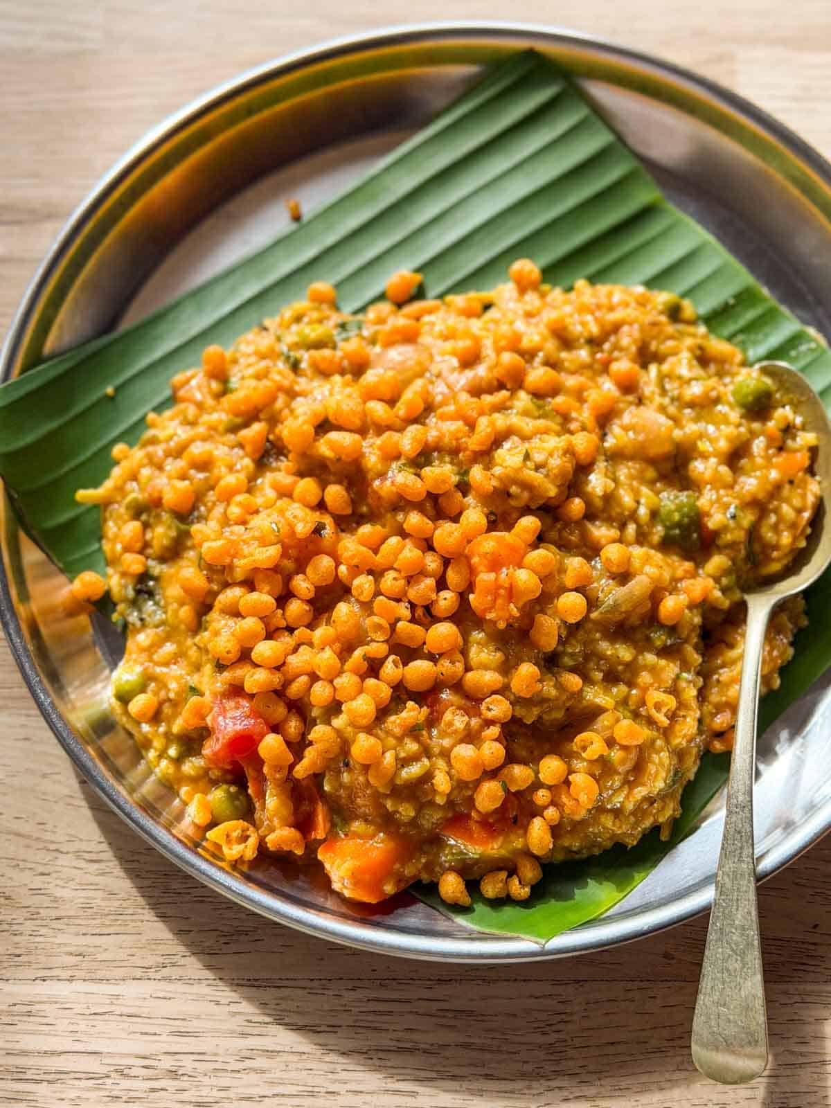 bisi bele bath topped with boondi and served on a plate lined with banana leaf