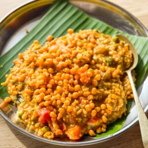 bisi bele bath topped with boondi and served on a plate lined with banana leaf