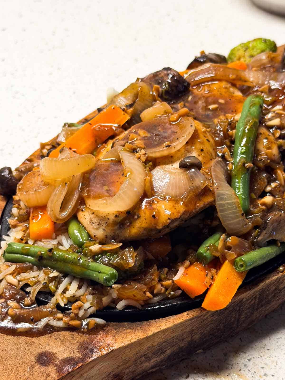 a close up image of chicken sizzler served n a sizzling tray ready to eat