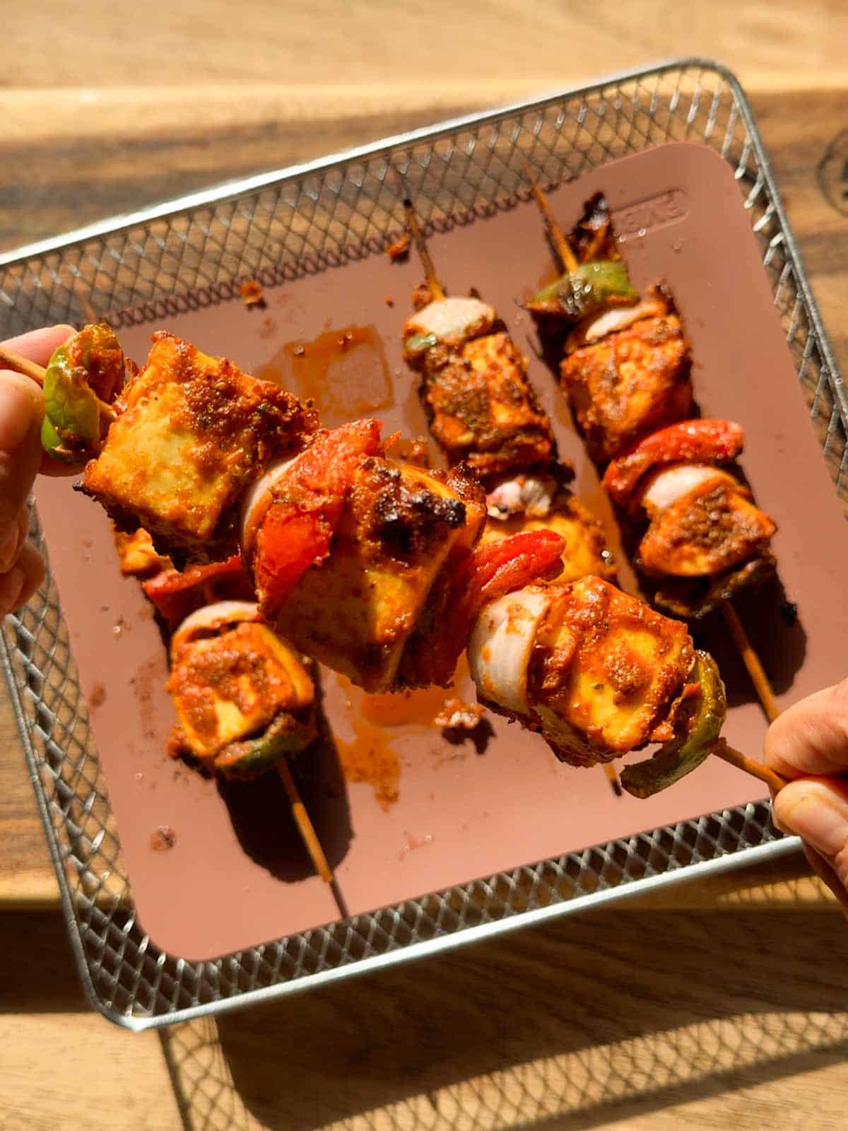 a person holding a skewer of air fryer paneer tikka to showcase its color and texture