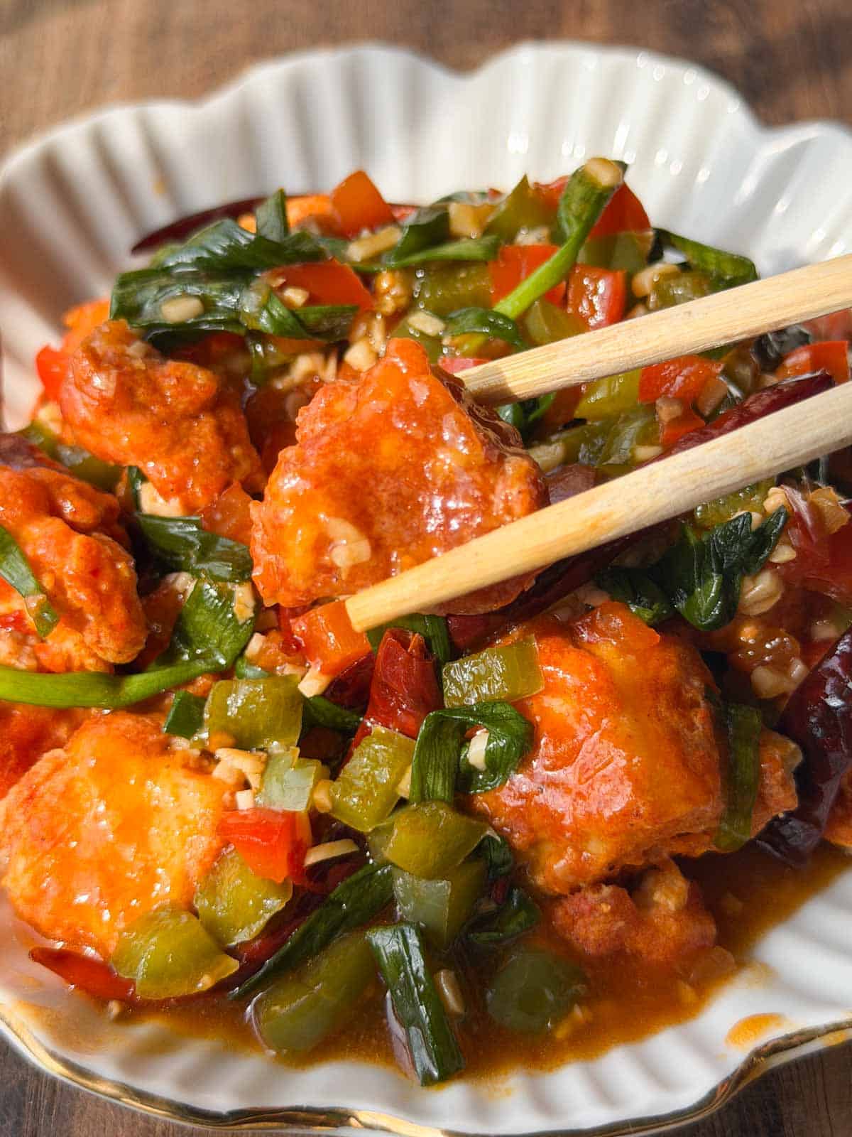 a close up image of crispy chili tofu served in a white bowl with chopsticks