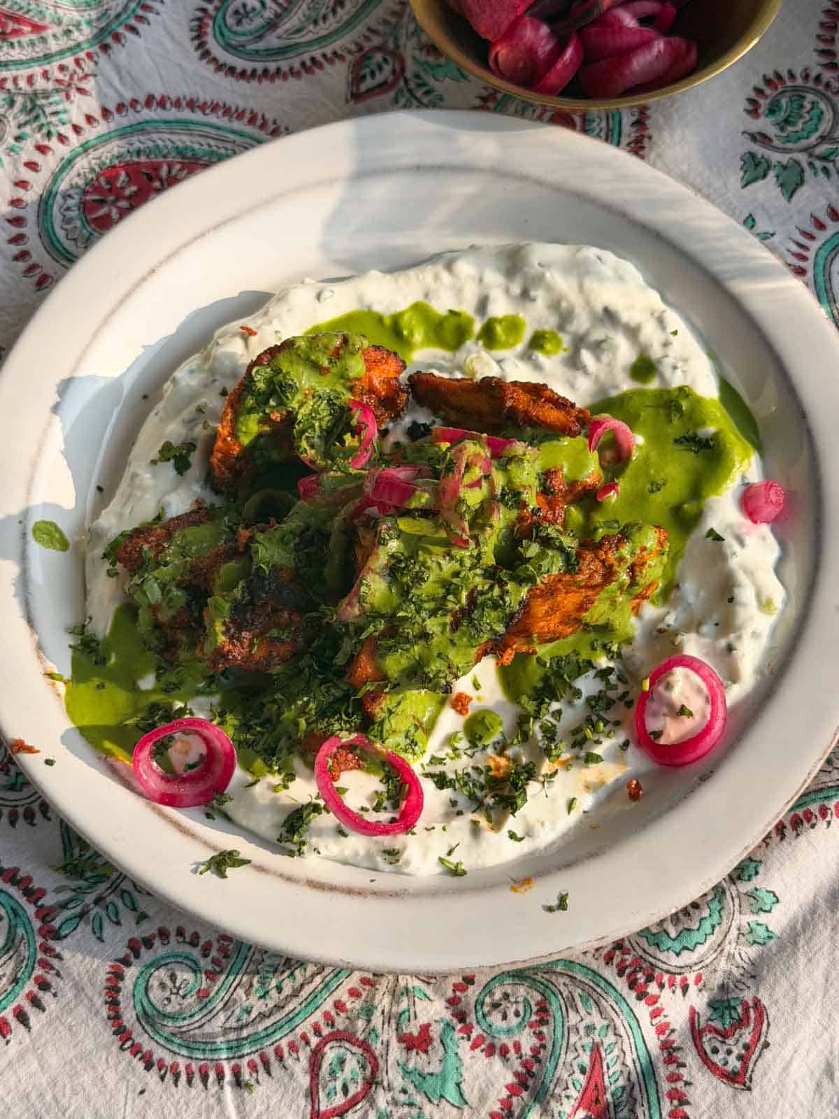 tandoori chicken served on top of curd and garnished with green chutney and onion rings